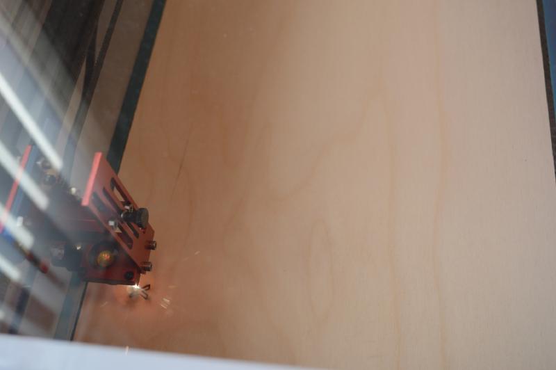 Laser cutter cutting an X into a piece of wood